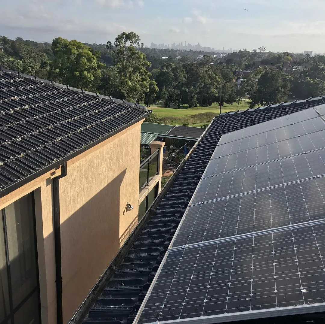 A clear gutter between a tile roof and solar panels, the city skyline in the distance